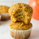 A stack of Whole Wheat Apple Muffins with a bite taken out of the top homemade muffin, showing the soft texture.