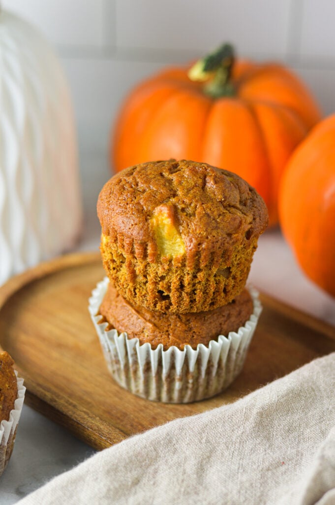 A stack of Apple Pumpkin Muffins with the paper liner taken off the top muffin to show its fluffy texture.