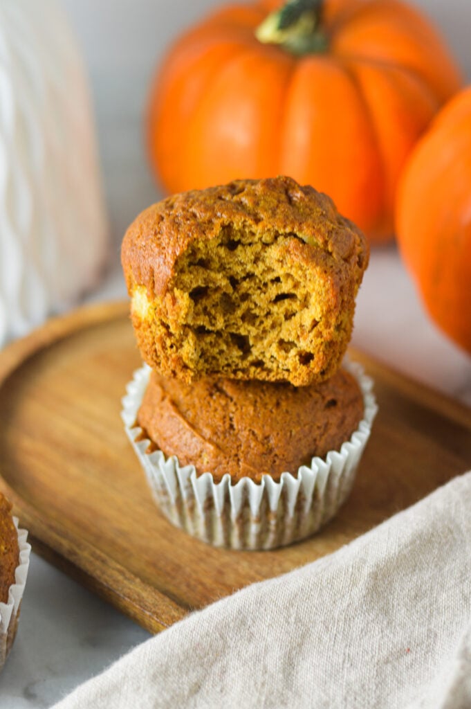 A stack of freshly baked Apple Pumpkin Muffins with a bite taken out the top muffin showing its soft interior.