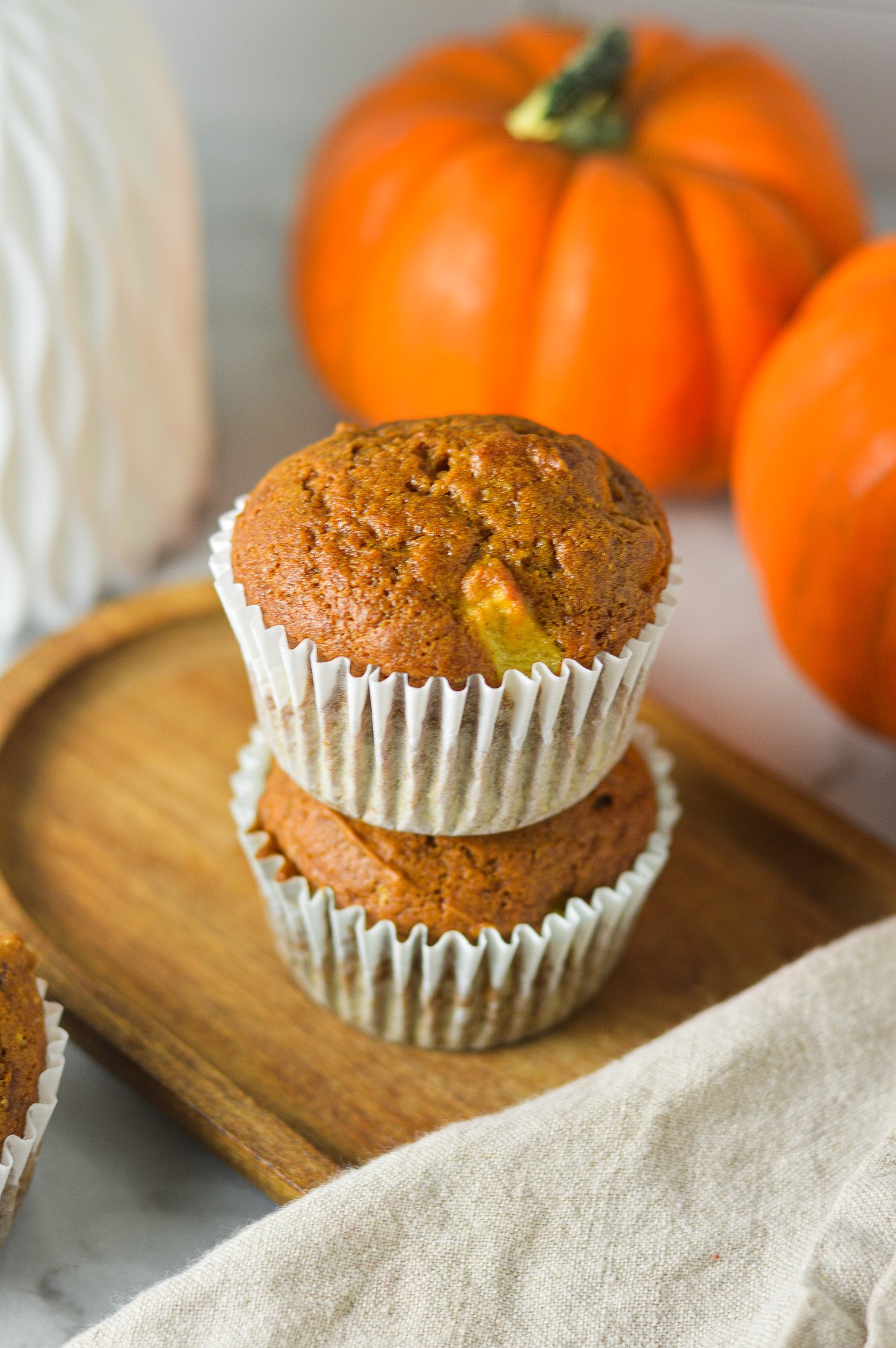 A stack of two golden brown Apple Pumpkin Muffins served on a rustic wooden tray with small pumpkins in the background.
