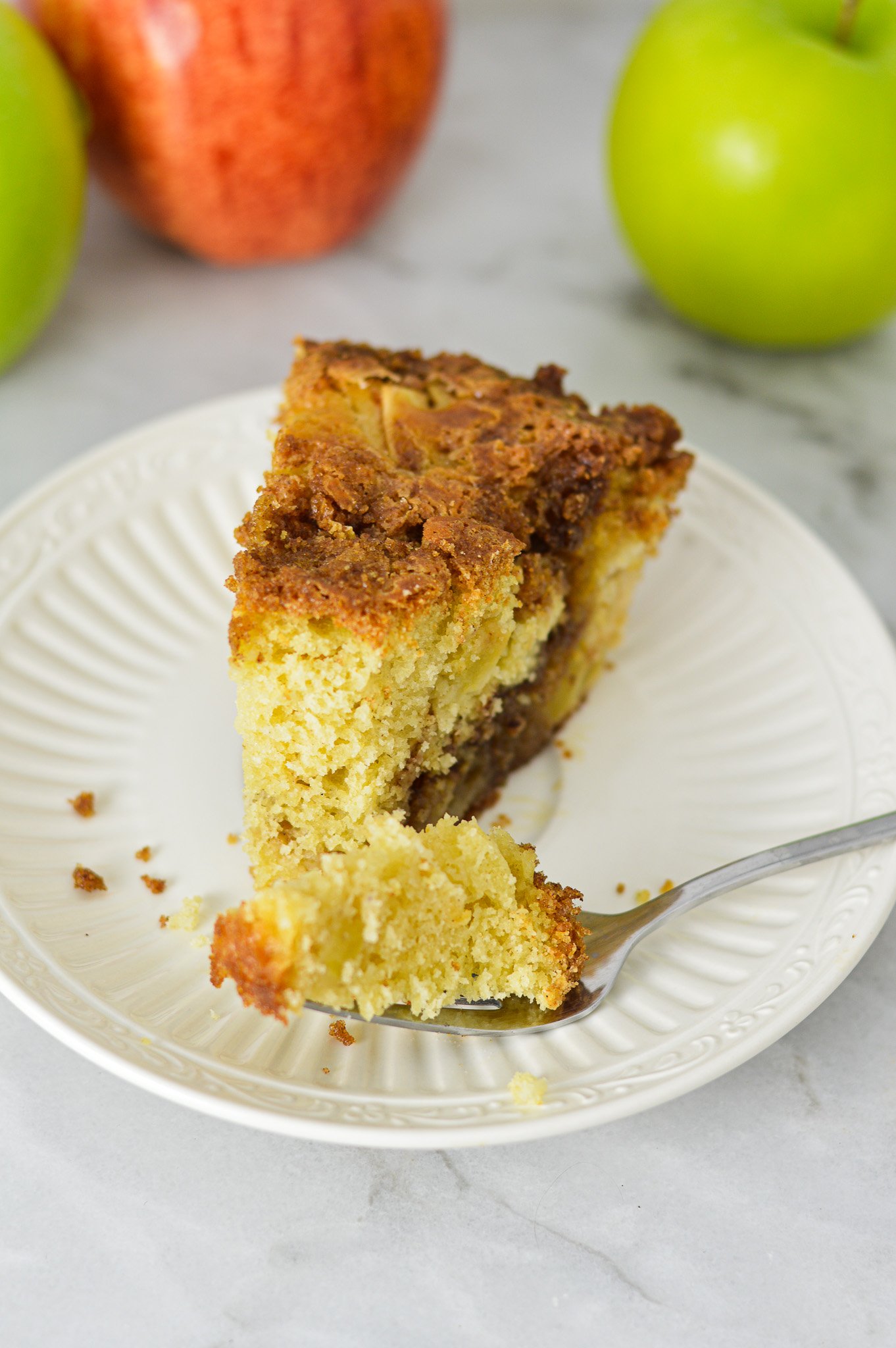 Easy Apple Coffee Cake on a small white plate with a forkful taken out, showing its fluffy texture.