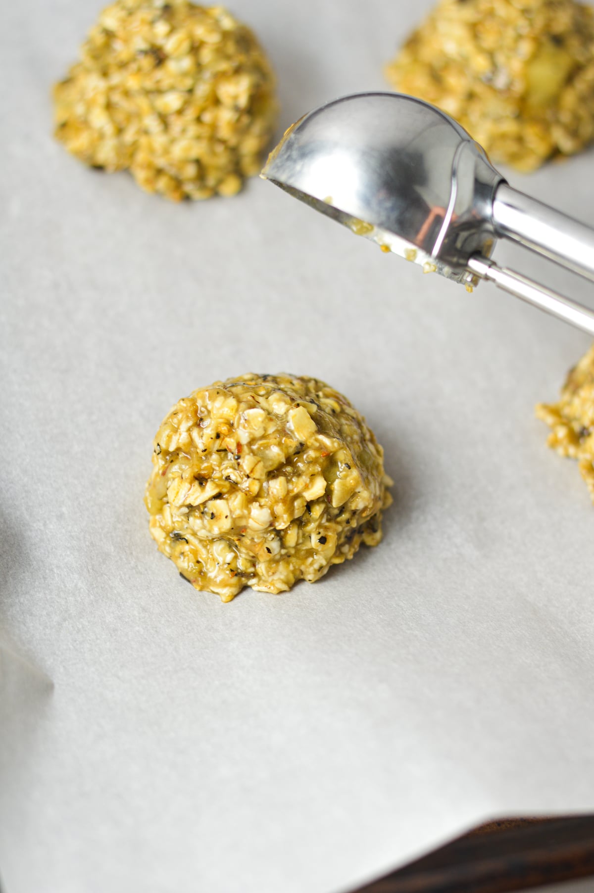 The banana chai latte cookie dough being scooped onto a parchment paper lined baking sheet using a medium cookie scoop.