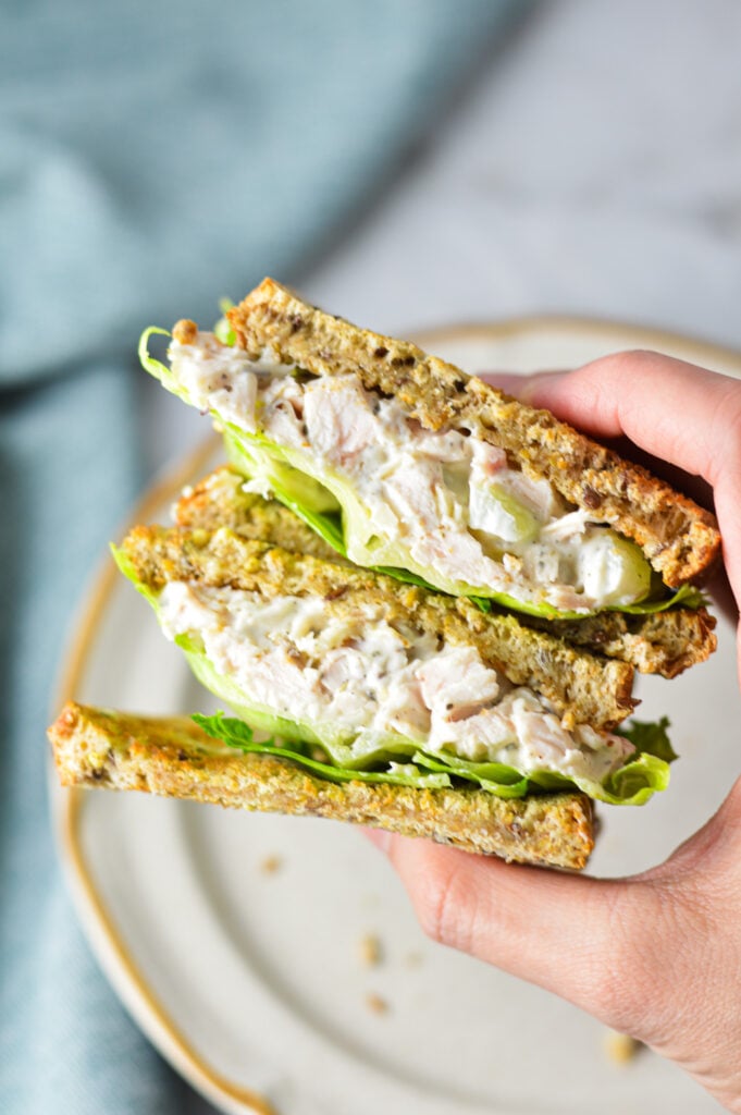 A hand holding up a Chicken Salad Sandwich cut in half.