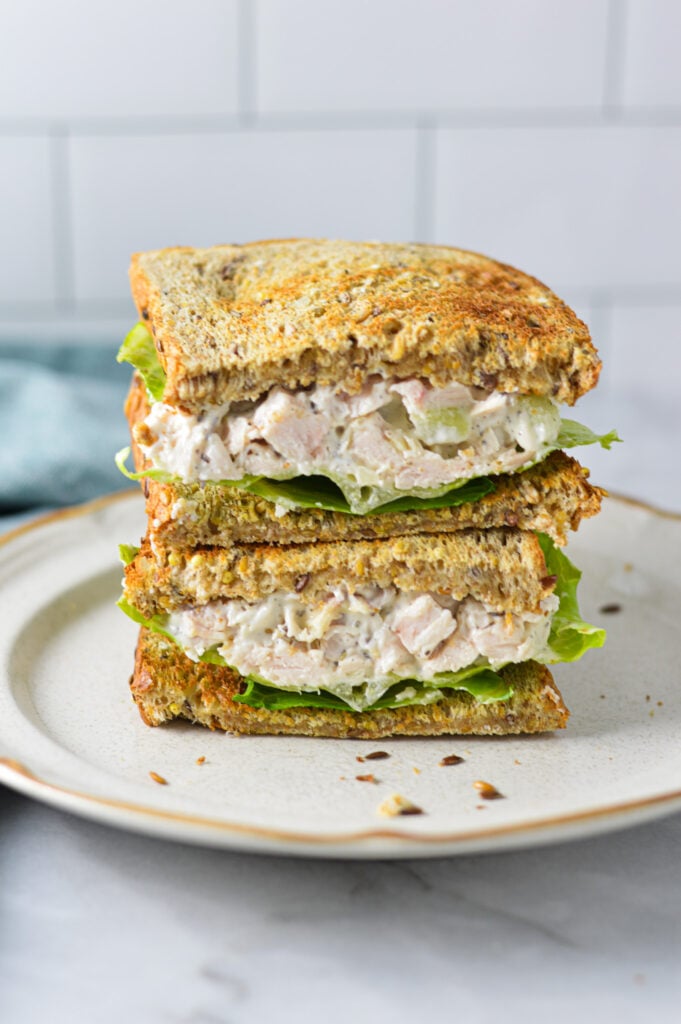 A Chicken Salad Sandwich on a small plate, with the lettuce and homemade chicken salad stuffed in between the whole wheat bread slices.
