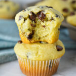 A stack of delicious Sour Cream Chocolate Chip Muffins with a bite taken out of the top muffin, showing its fluffy texture and melty chocolate chips.