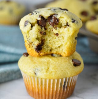 A stack of delicious Sour Cream Chocolate Chip Muffins with a bite taken out of the top muffin, showing its fluffy texture and melty chocolate chips.