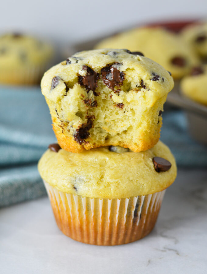 A stack of delicious Sour Cream Chocolate Chip Muffins with a bite taken out of the top muffin, showing its fluffy texture and melty chocolate chips.