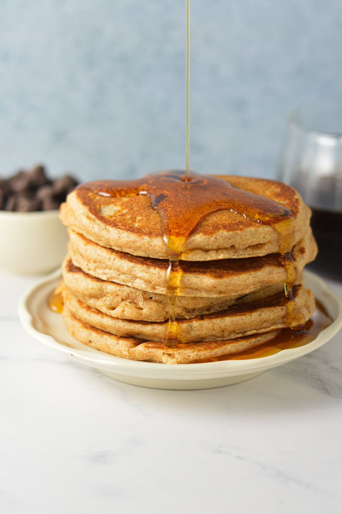 A stack of fluffy whole wheat chocolate chip pancakes being drizzled with pure maple syrup.
