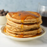 A tall stack of golden-brown Whole Wheat Chocolate Chip Pancakes loaded with melty chocolate chips and warm maple syrup poured on top.