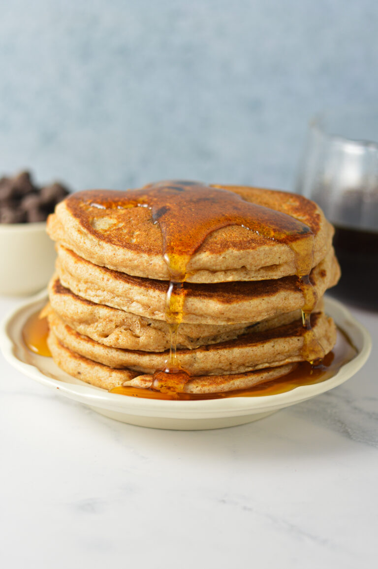 A tall stack of golden-brown Whole Wheat Chocolate Chip Pancakes loaded with melty chocolate chips and warm maple syrup poured on top.