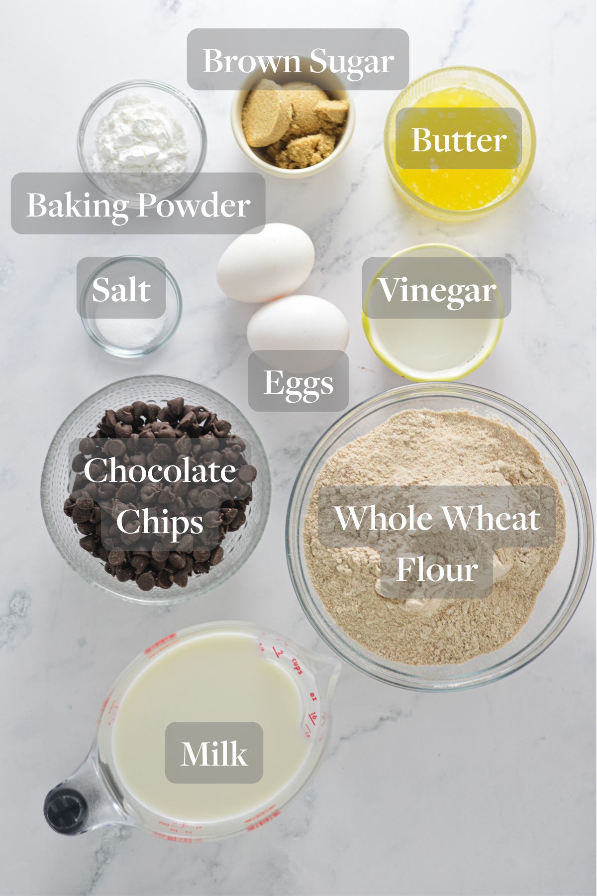 All of the ingredients needed to make Whole Wheat Chocolate Chip Pancakes laid out on a marble surface.