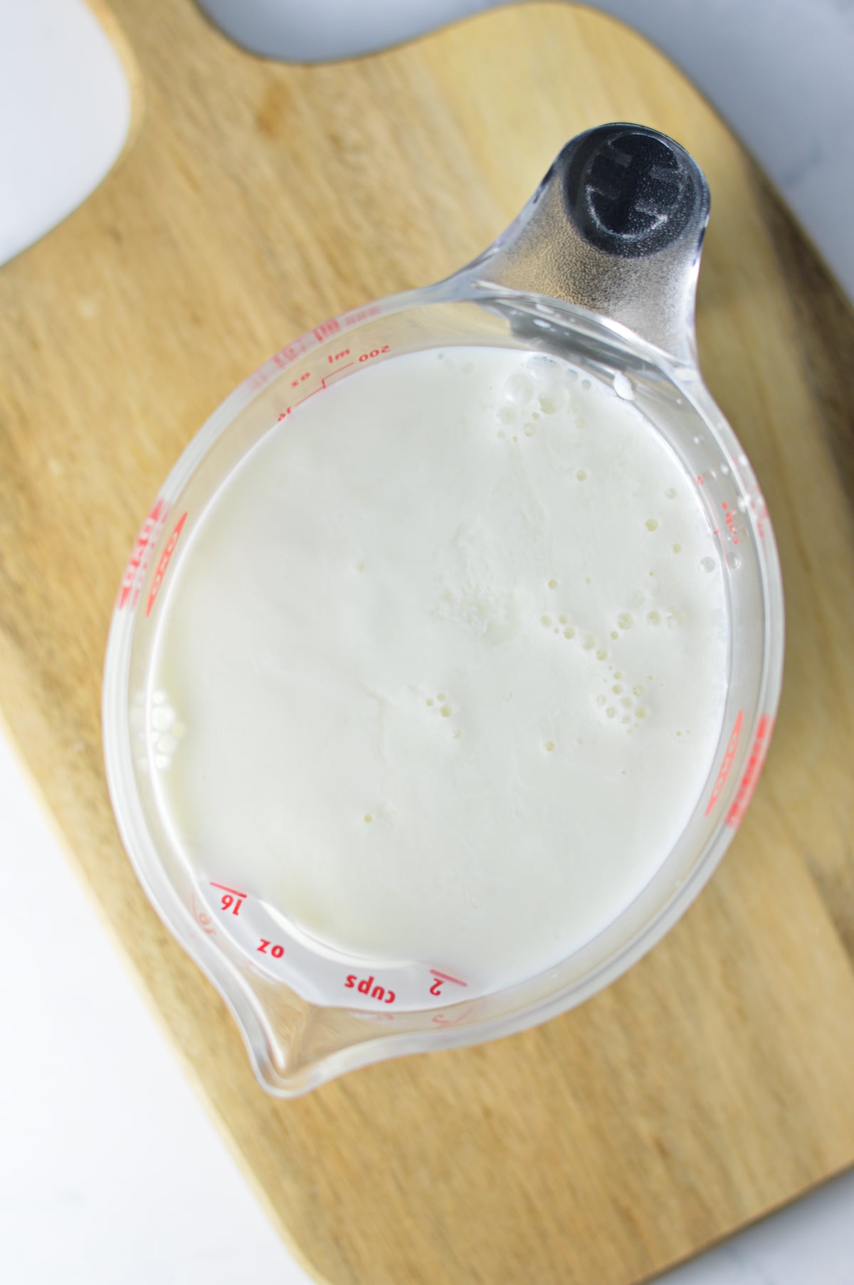 Some milk in a pourable measuring cup being soured by white vinegar.