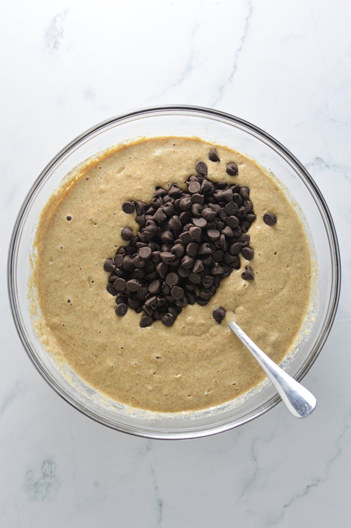 A large glass bowl with the Whole Wheat Pancake batter with some semi-sweet chocolate chips resting on top of the fluffy batter.