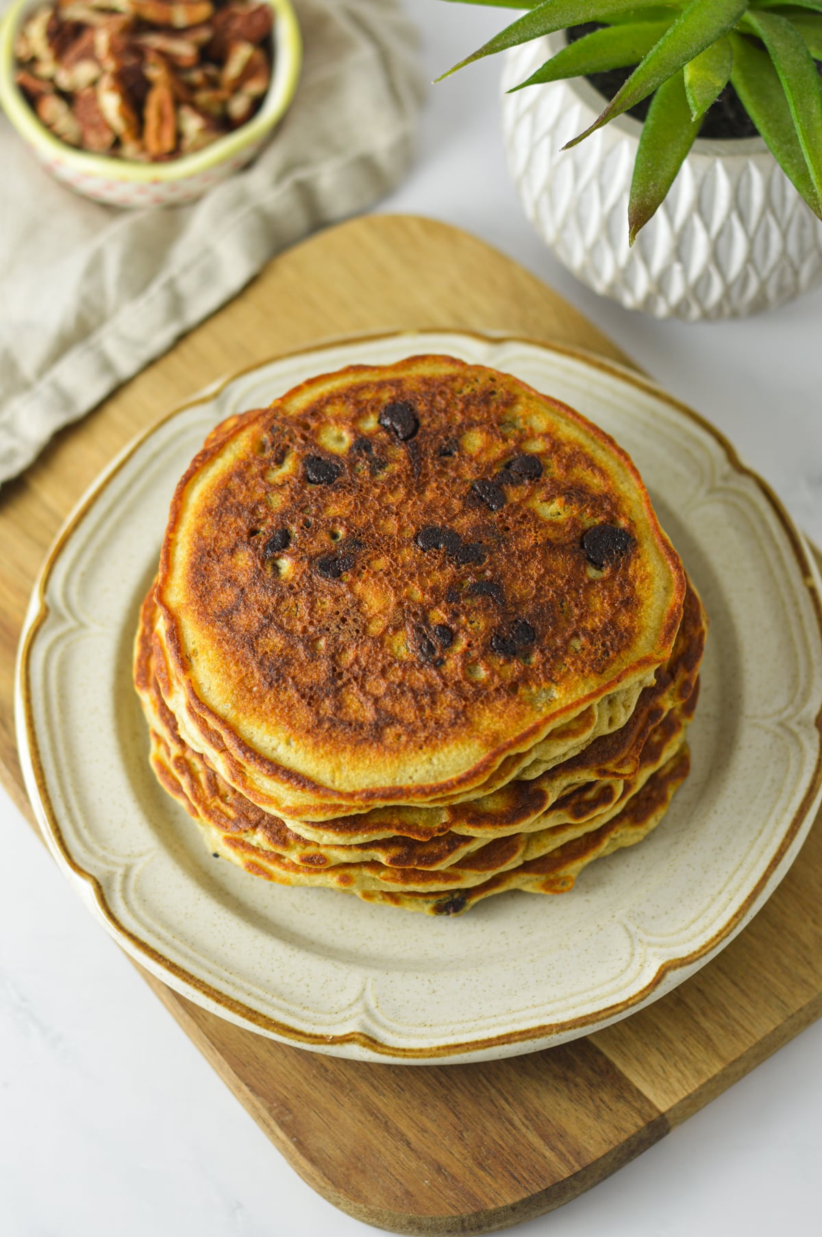 Top-down view of a golden-brown pancake stack drizzled with syrup and sprinkled with chocolate chips and pecans.