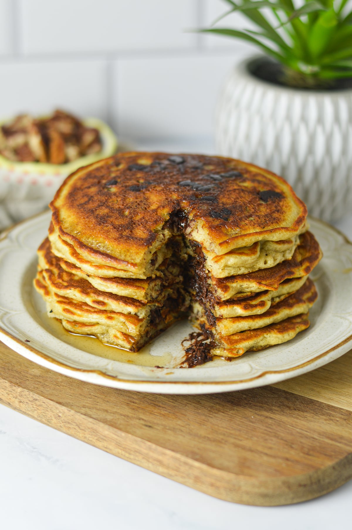 A stack of golden-brown pancakes cut open to reveal layers filled with melted chocolate chips and pecans, served on a white plate with syrup dripping down the sides.
