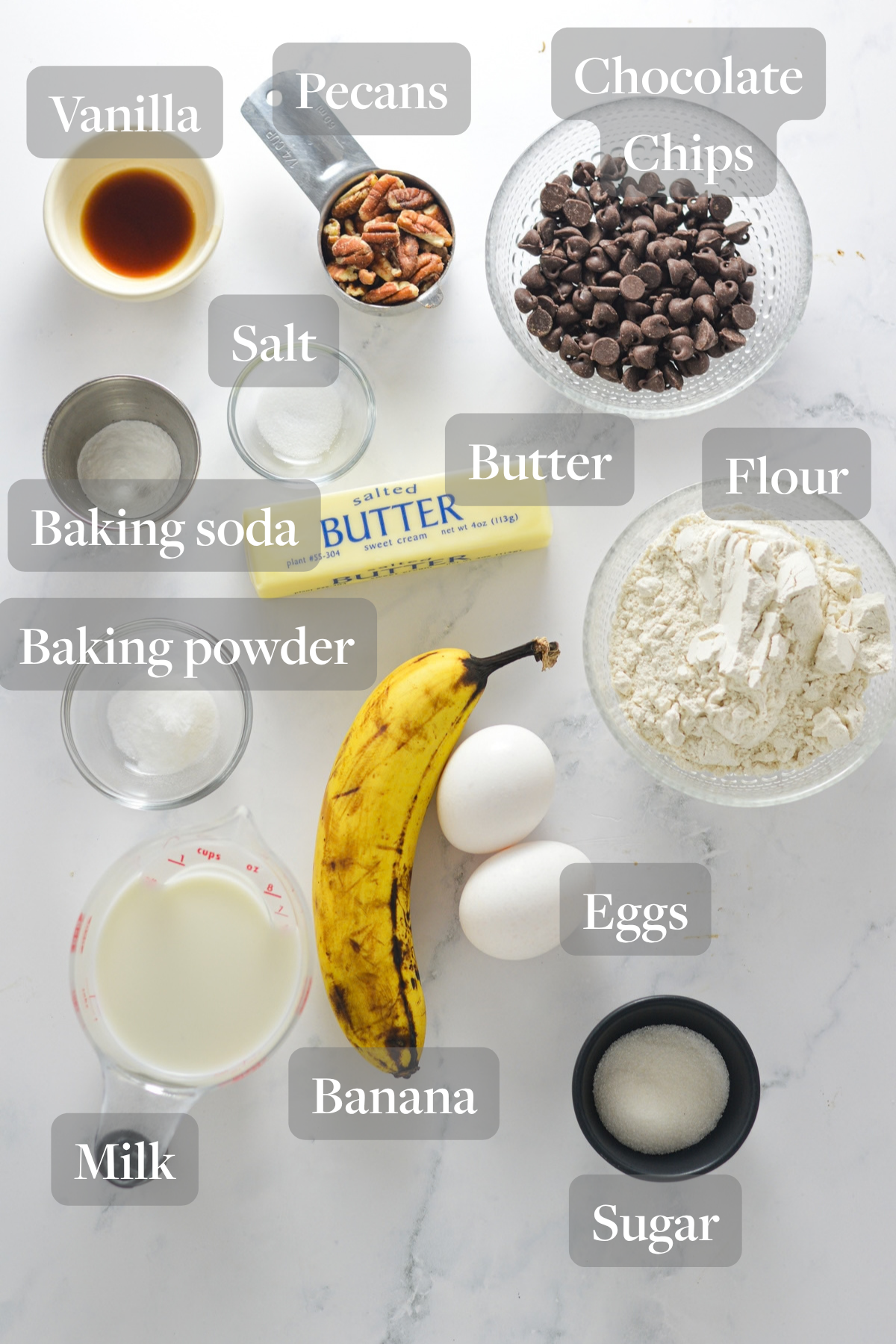 All the ingredients you need to make Chocolate Chip Banana Pecan Pancakes laid out on a marble surface.