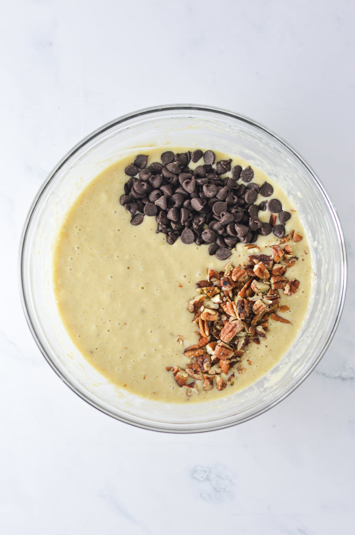 The Chocolate Chip Banana Pecan Batter in a large bowl, with the semi sweet chocolate chips and pecans resting on top of the pourable batter.