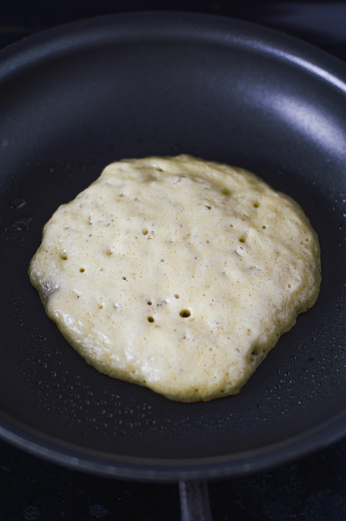 A Chocolate Chip Banana Pecan Pancake being cooked on a medium skillet.