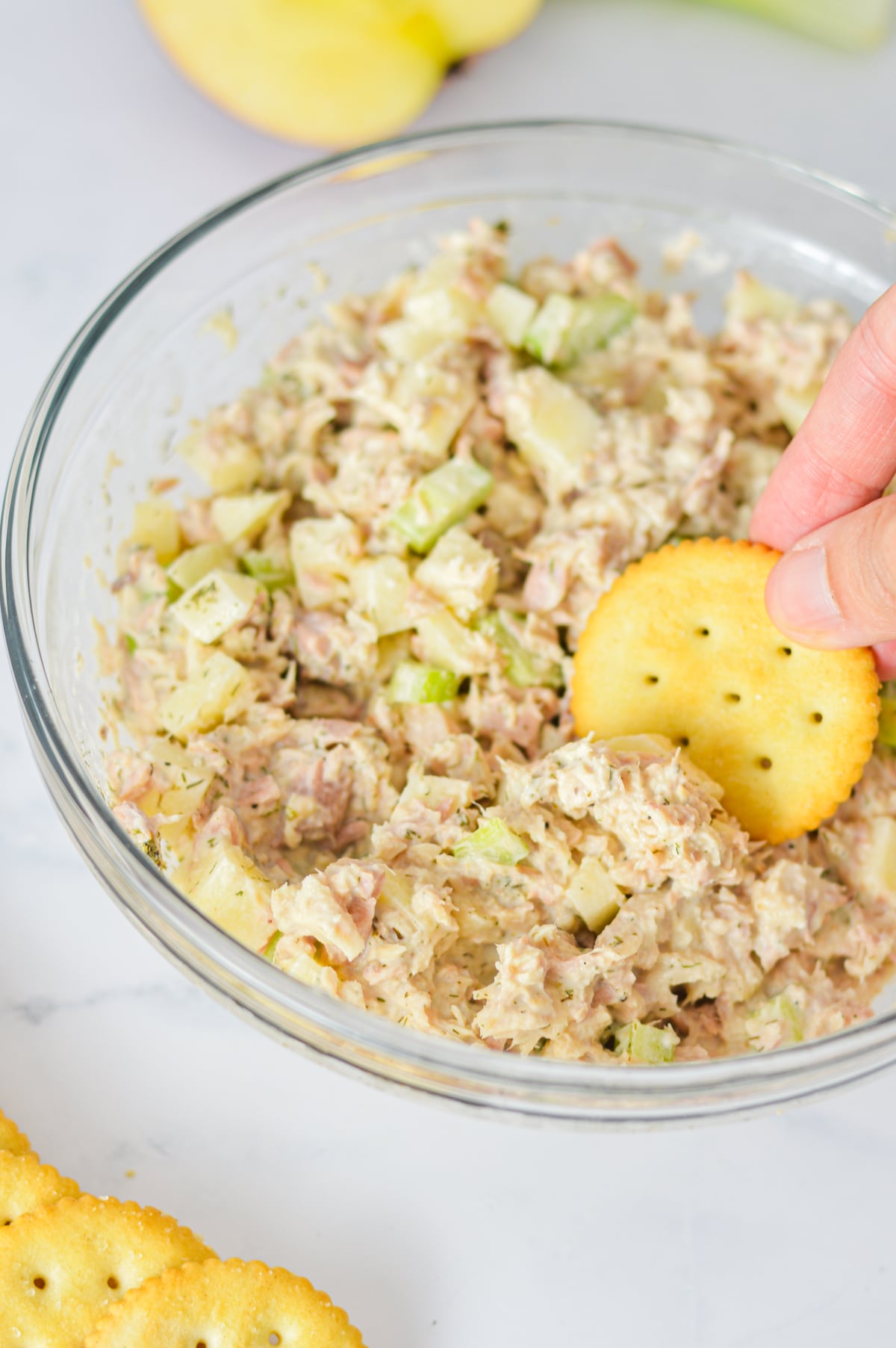 Apple Tuna Salad in a glass bowl, with a hand dipping a Ritz cracker into the creamy tuna salad.