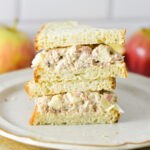 Apple Tuna Salad Sandwich sliced in half and stacked on a plate, with some fresh apples in the background.