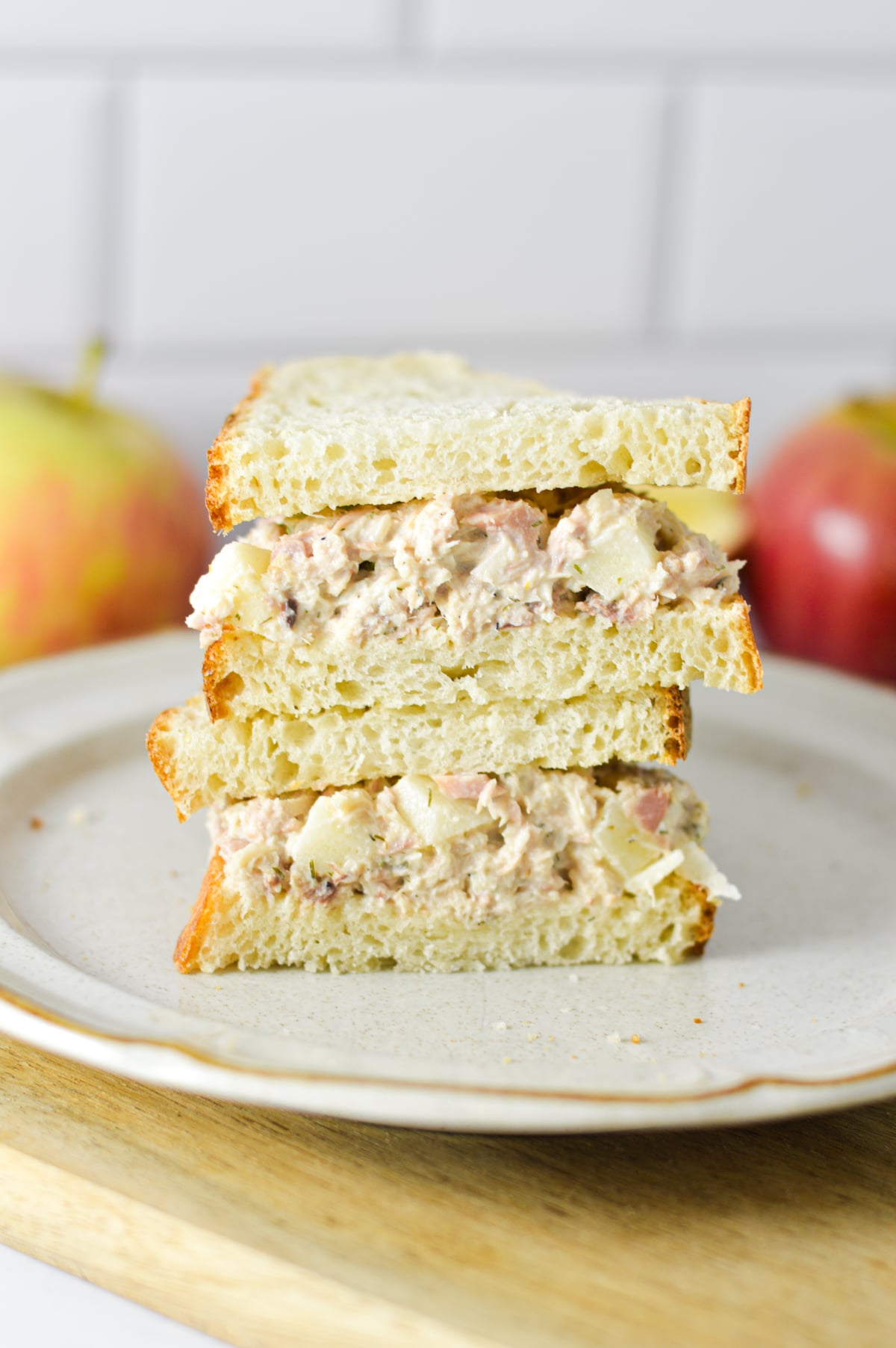 Apple Tuna Salad Sandwich sliced in half and stacked on a plate, with some fresh apples in the background.