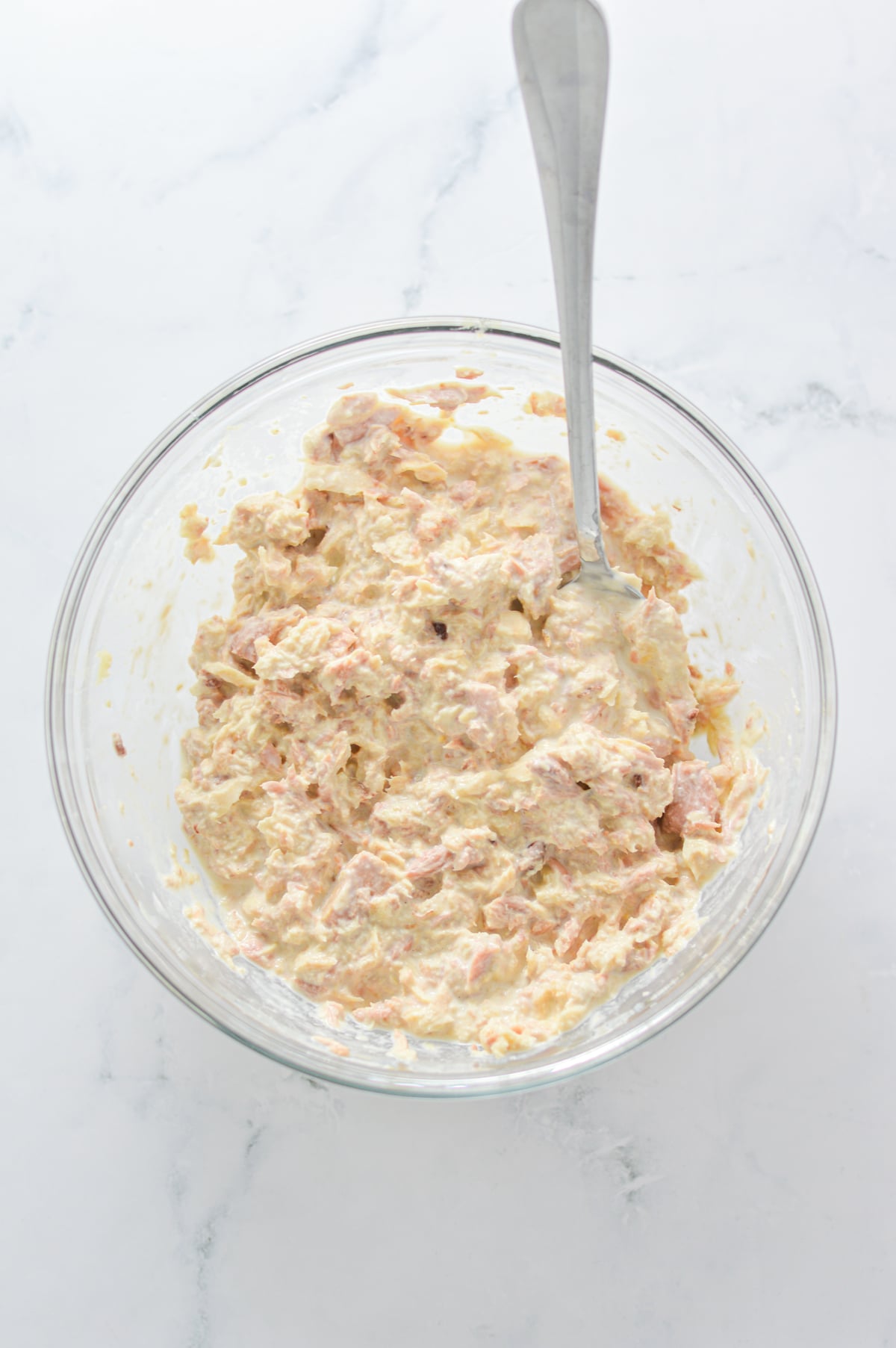 Canned tuna, mayonnaise and lemon juice mixed together in a medium bowl, with a spoon sticking out of it.