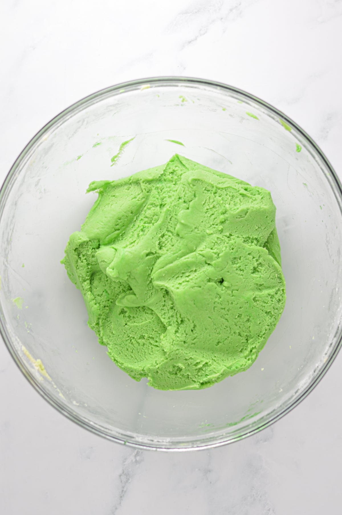 The green cookie dough of the witch finger cookies mixed up in a large glass bowl.