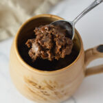 A spoonful of rich, fudgy microwave brownie being lifted out of a ceramic mug filled with single-serving chocolate brownie.