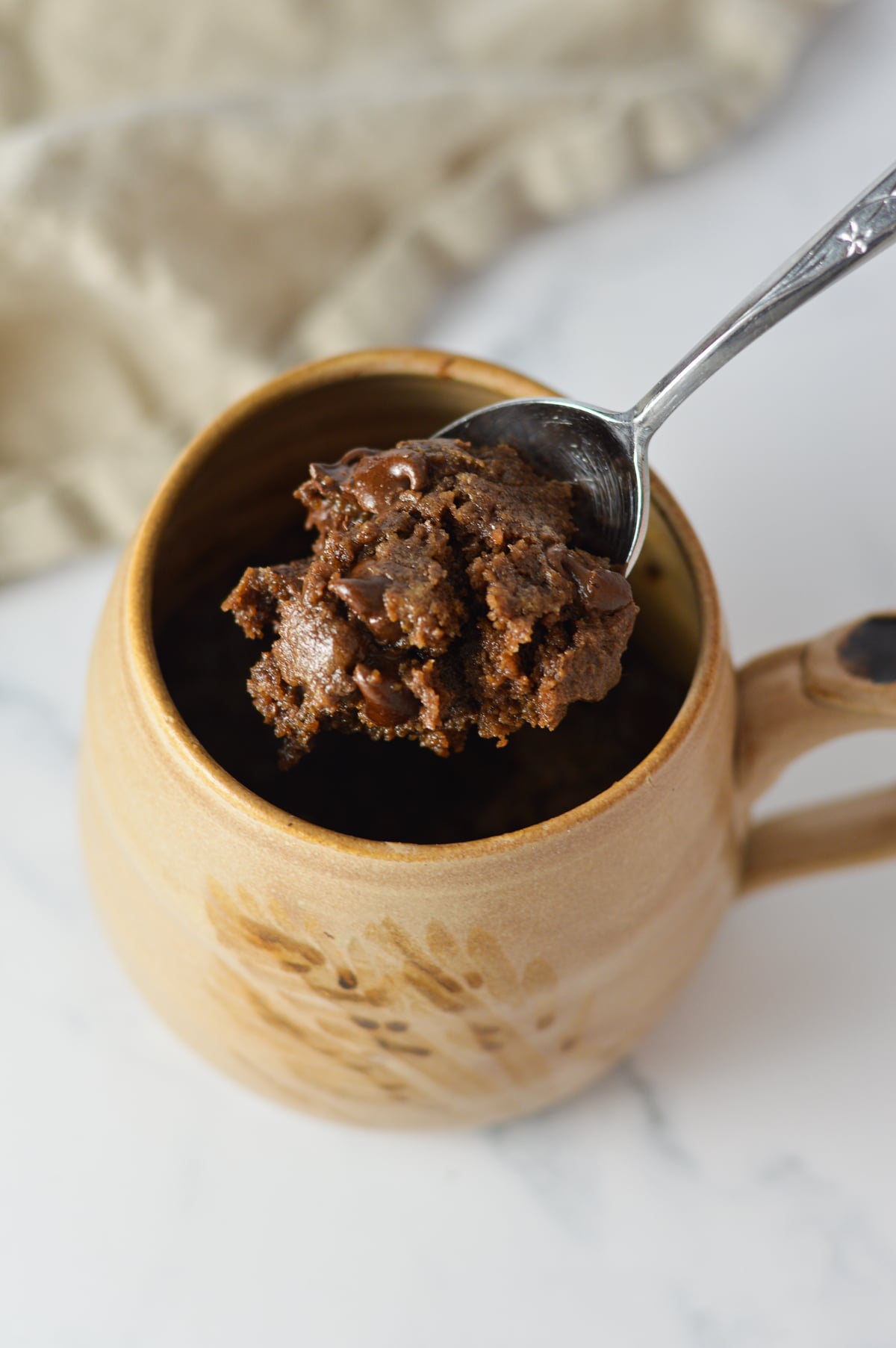 A spoonful of rich, fudgy microwave brownie being lifted out of a ceramic mug filled with single-serving chocolate brownie.