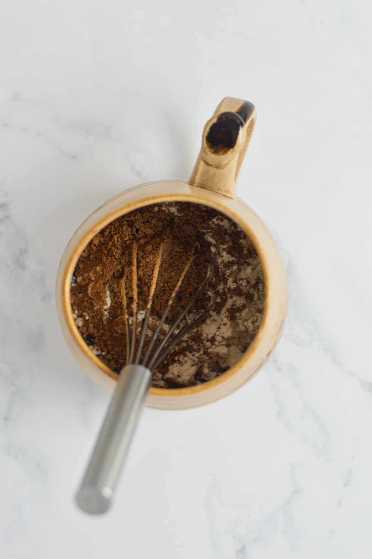 A small whisk in a large mug mixing the ingredients to make a single-serve microwave brownie.