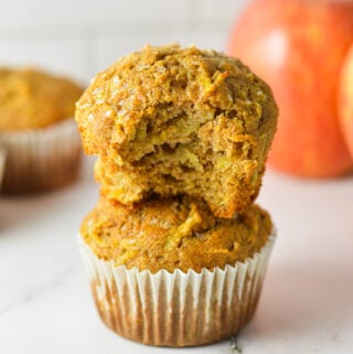 Golden brown Apple Streusel Muffins topped with a crumbly cinnamon sugar topping, stacked on a granite surface with fresh apples in the background.