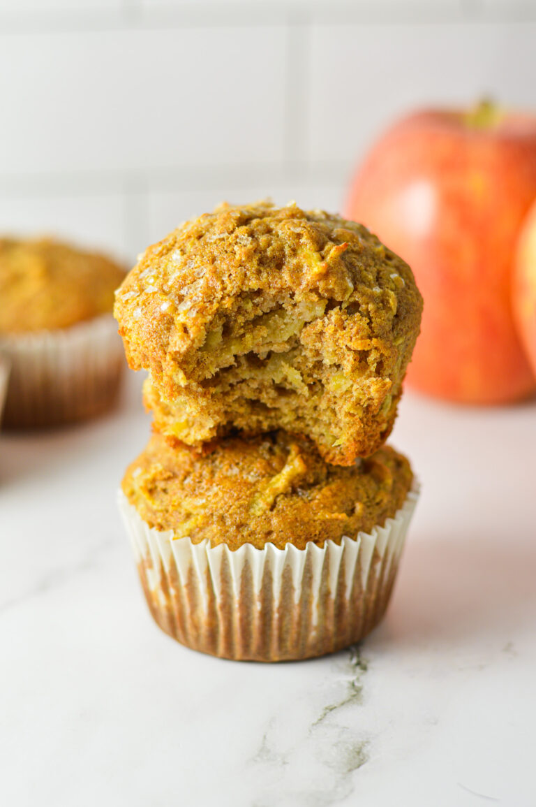 Golden brown Apple Streusel Muffins topped with a crumbly cinnamon sugar topping, stacked on a granite surface with fresh apples in the background.