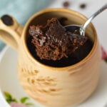 Single-serve chocolate mug cake garnished with melted chocolate chips in a cream ceramic mug served on a small plate.