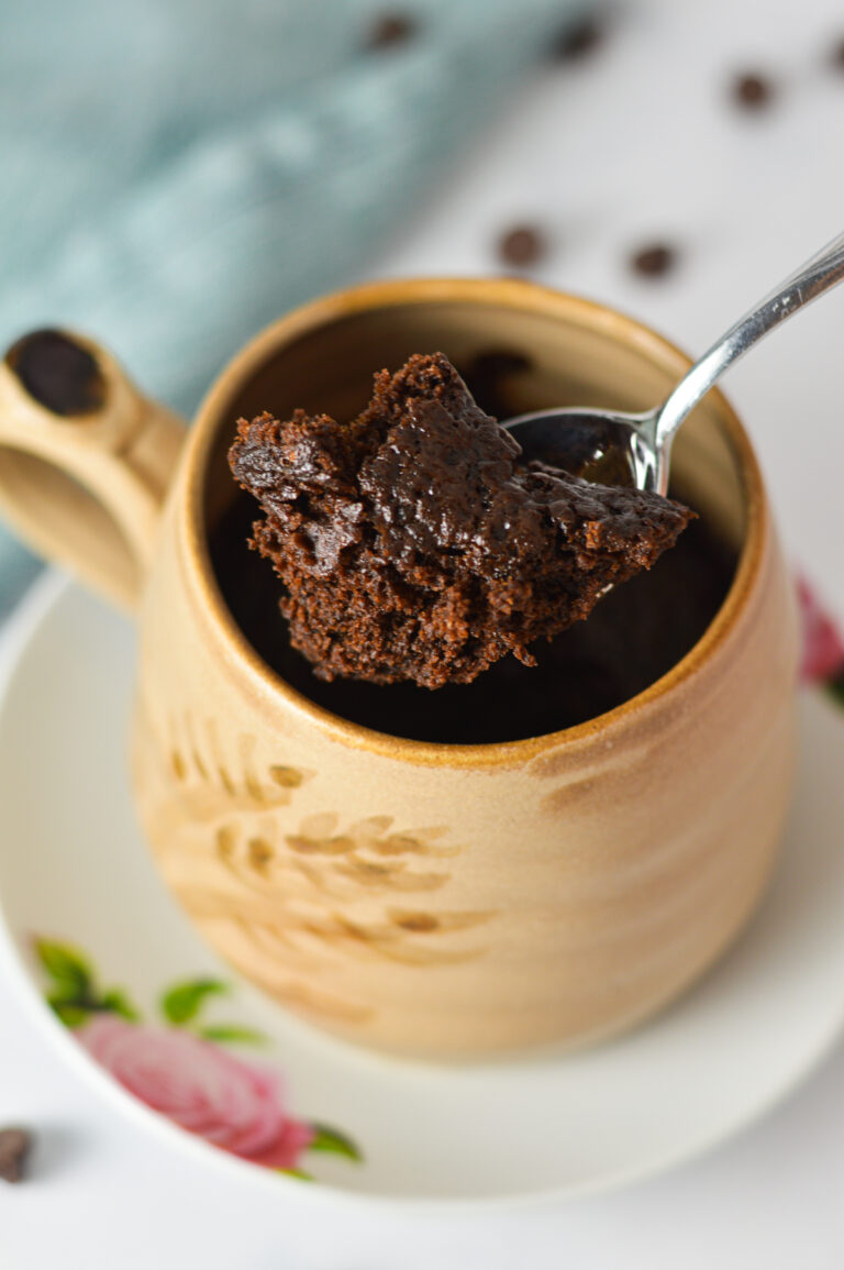 Single-serve chocolate mug cake garnished with melted chocolate chips in a cream ceramic mug served on a small plate.