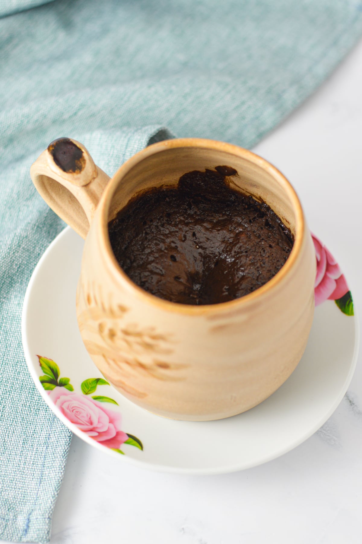 Freshly made chocolate mug cake in a beige ceramic mug on a floral saucer.