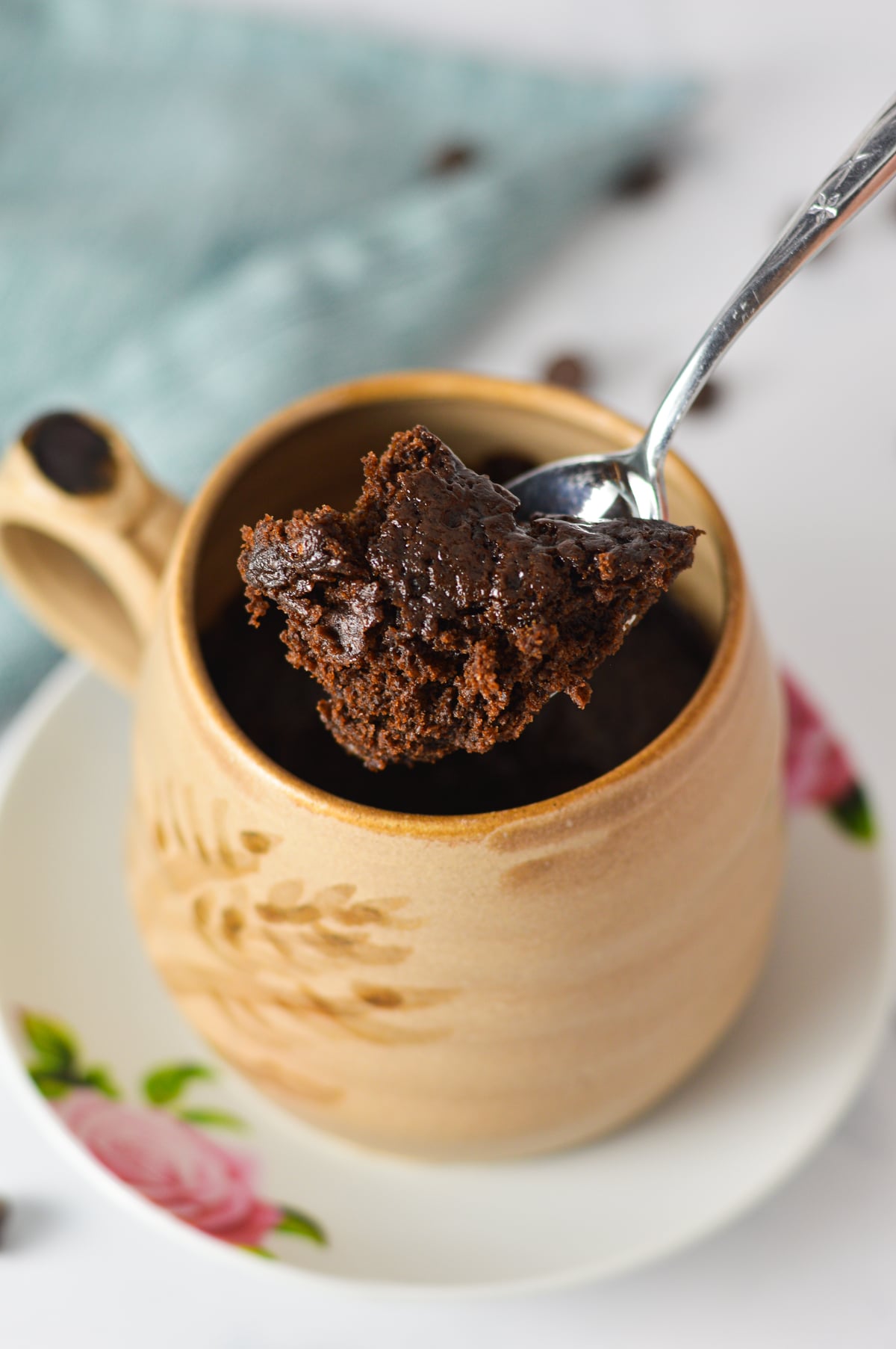 A spoon scooping into a freshly baked chocolate mug cake in a beige ceramic mug.