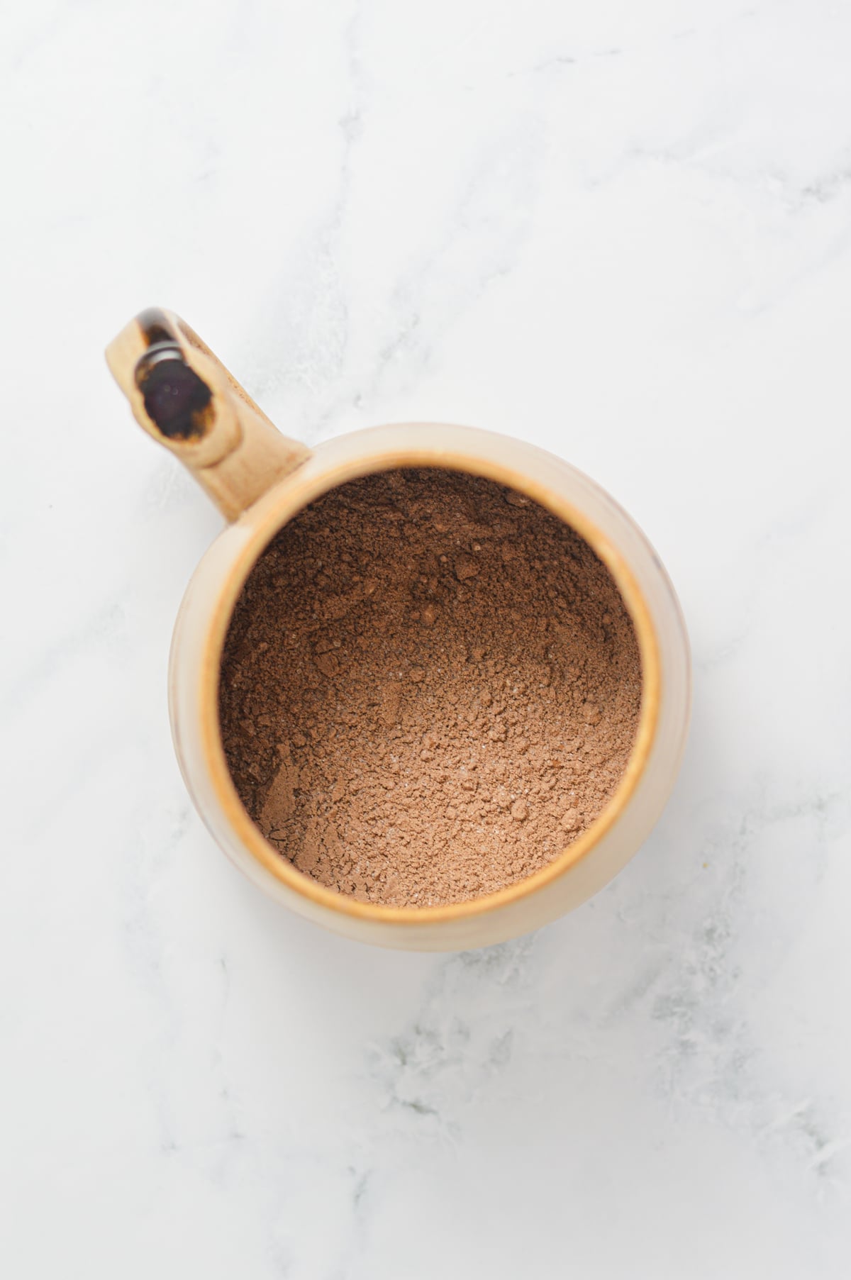A large ceramic mug filled with the dry ingredients of a chocolate mug cake.
