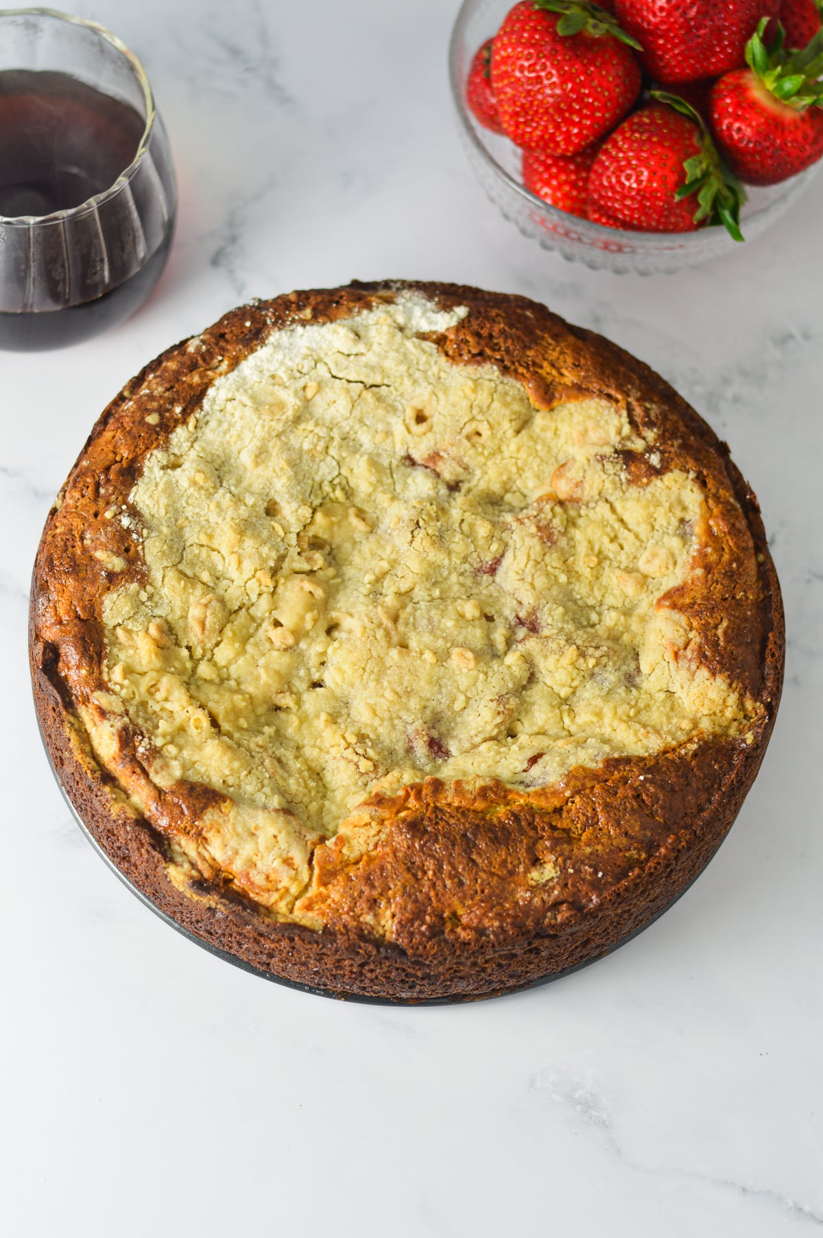 A freshly baked, whole strawberry cream cheese coffee cake with a golden-brown crumb topping, shown straight out of the oven in a springform pan.