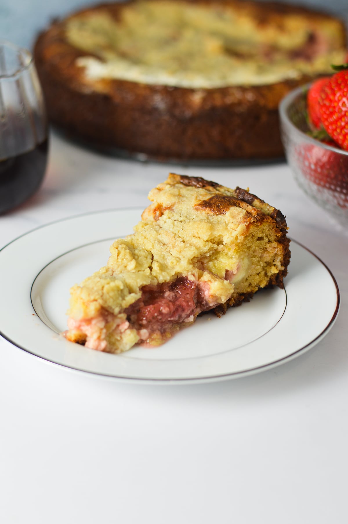A close-up of a single slice of strawberry cream cheese coffee cake served on a white plate, highlighting the moist cake layers, creamy cheesecake filling, and sweet strawberry swirl.