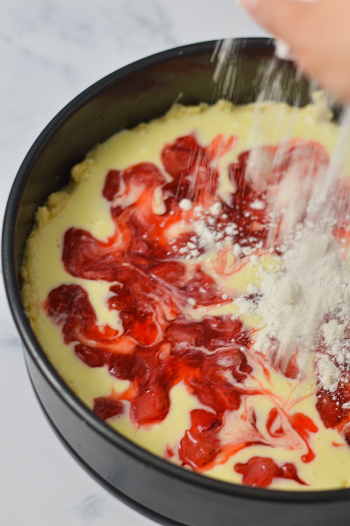 The unbaked Strawberry Cream Cheese Coffee Cake batter in a springform pan, with some of the crumb topping being sprinkled on top.