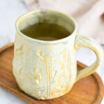Apple Cider Vinegar Tea in a large green ceramic mug on a small wooden surface.