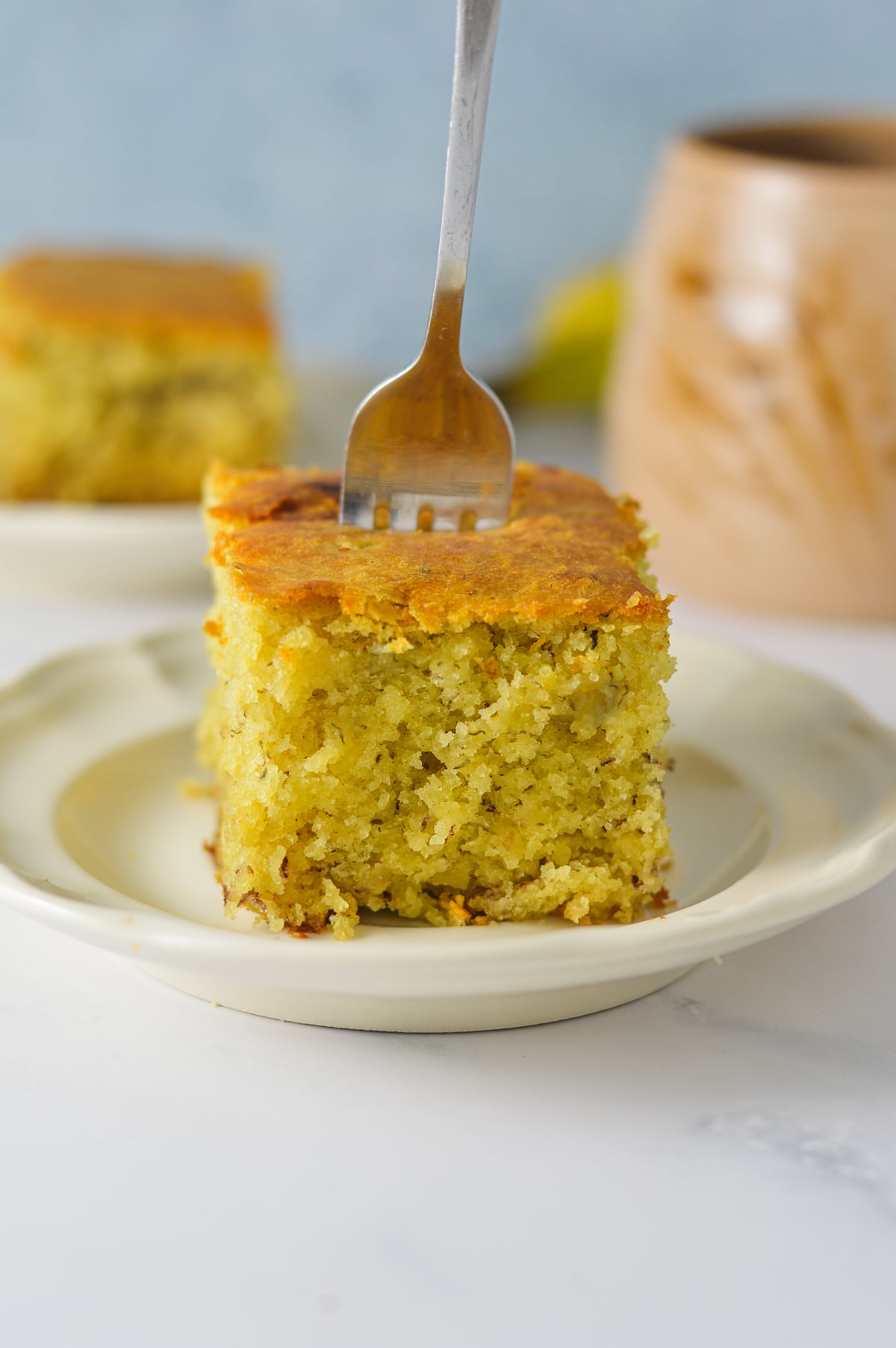 A slice of Banana Vanilla Cake on a small plate, with a fork sticking out of the moist cake.