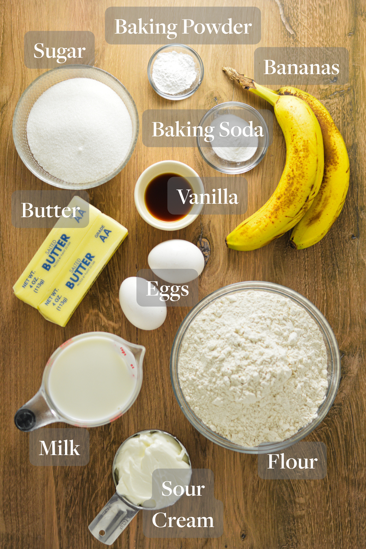 All the ingredients you need to make Banana Vanilla Cake laid out on a wooden surface.