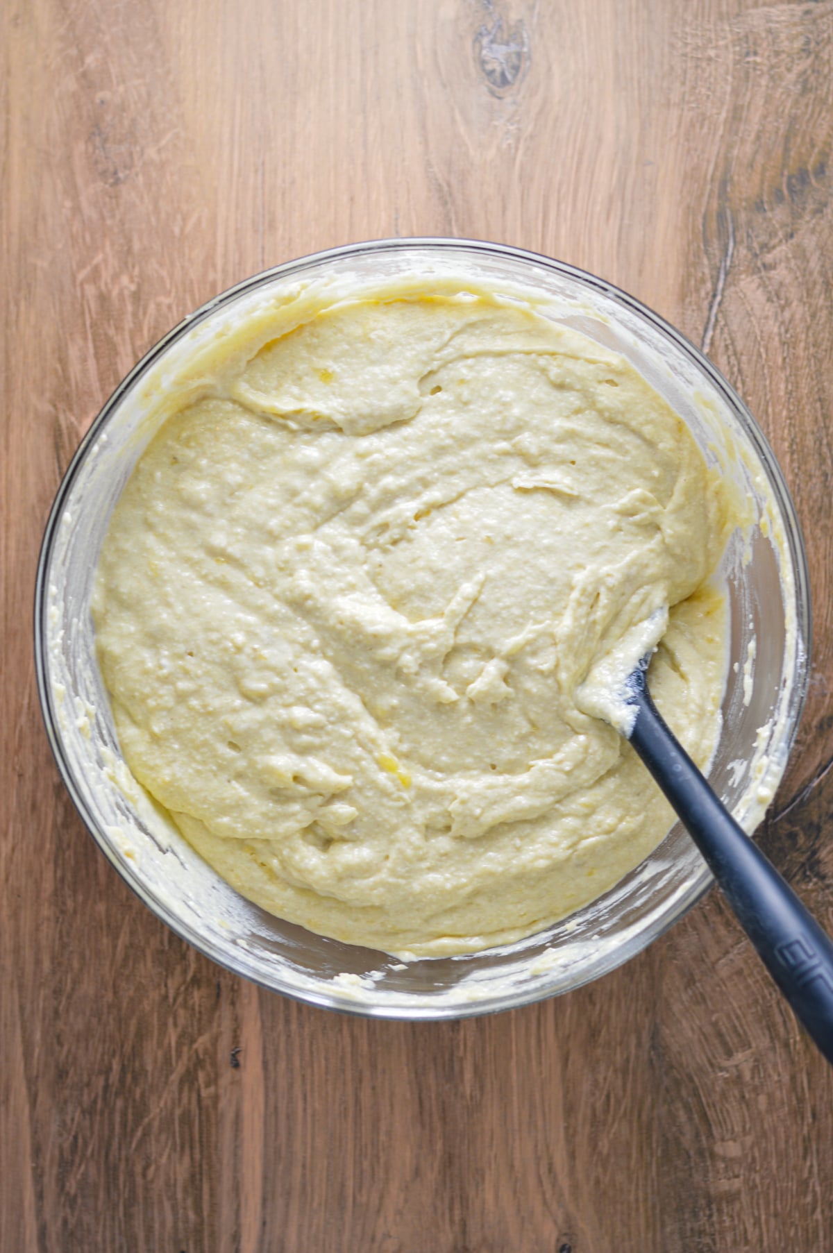All of the ingredients for a Banana Vanilla Cake mixed together in a glass bowl with a rubber spatula in the batter.