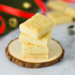 A stack of Shortbread Cookies cut into small rectangles, with Christmas decorations in the background.