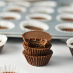 Three mini Nutella fudge cups stacked with their paper liners removed next to a mini muffin tin filled with fudge cups.
