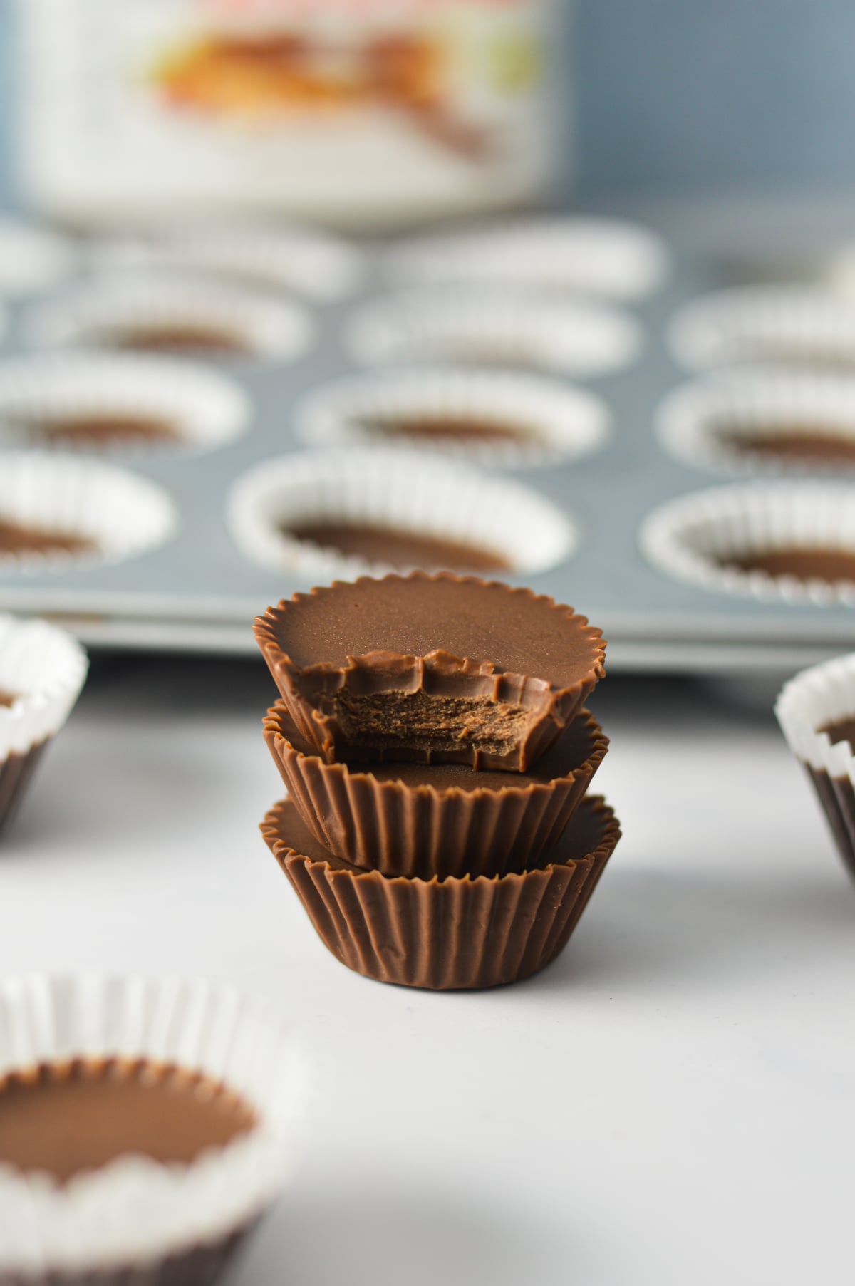 Three mini Nutella fudge cups stacked with their paper liners removed next to a mini muffin tin filled with fudge cups.