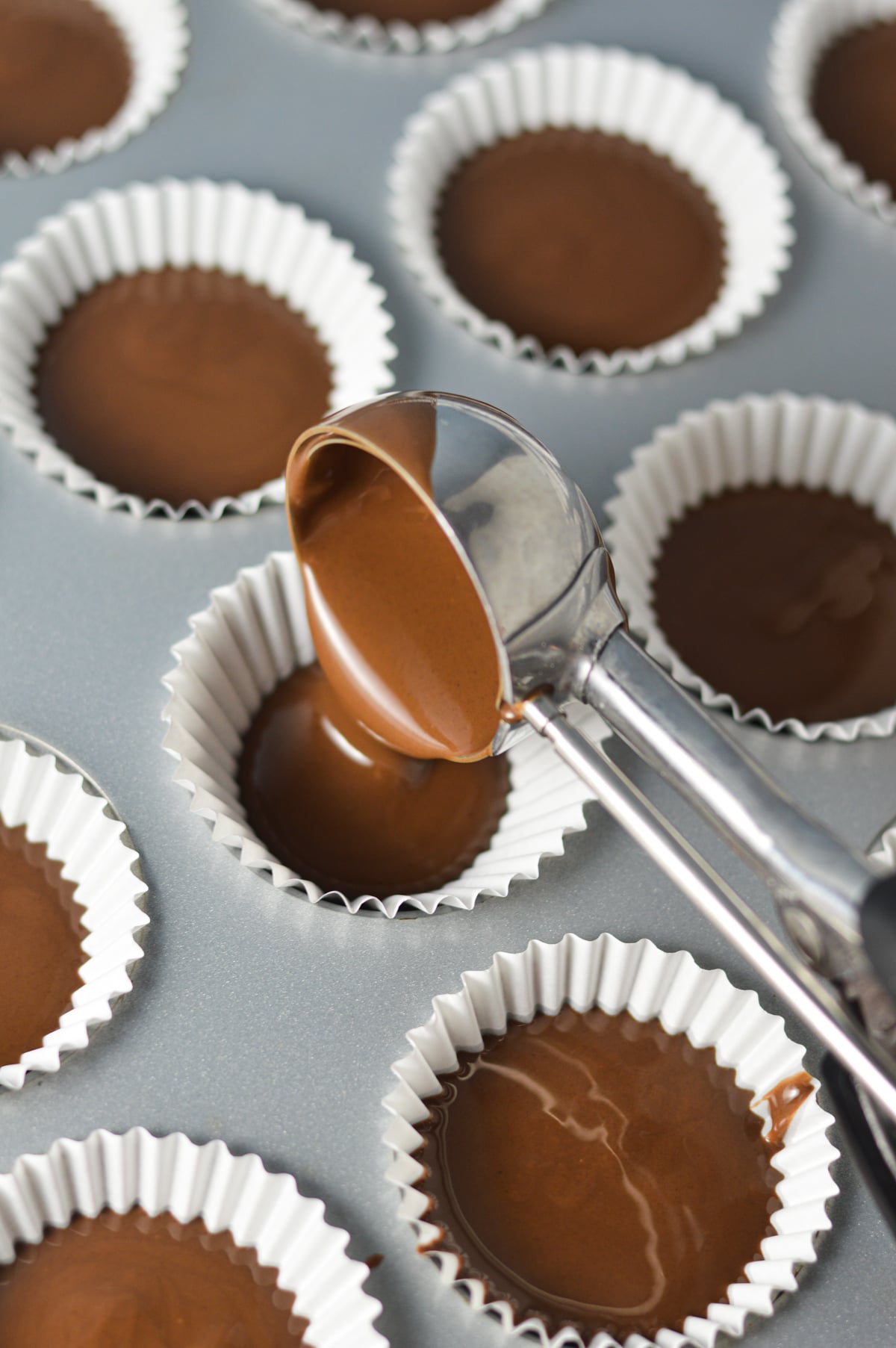 A medium cookie scoop dividing the Nutella mixture in a mini muffin pan lined with mini paper liners.