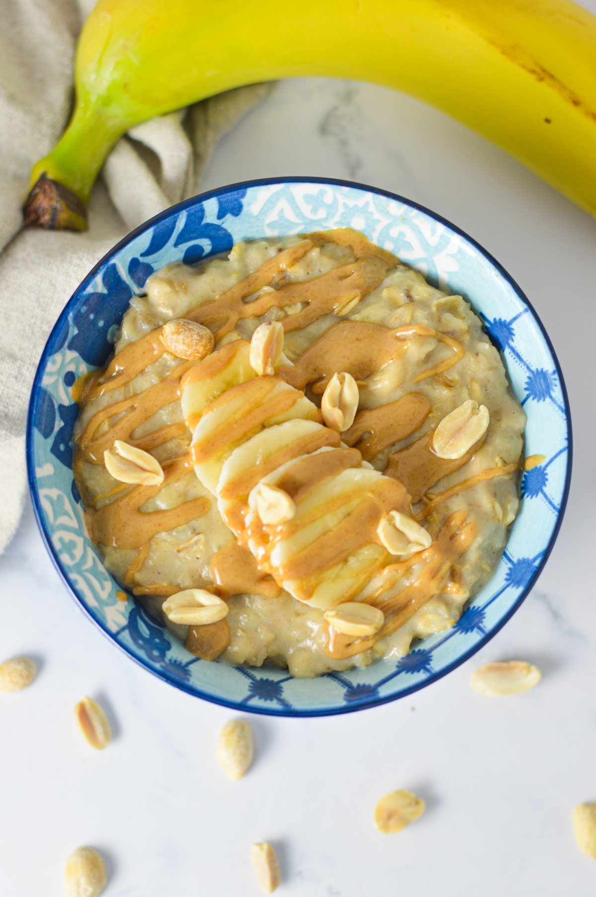 A bowl of warm peanut butter and banana oatmeal topped with sliced bananas, chopped peanuts, and a drizzle of peanut butter.
