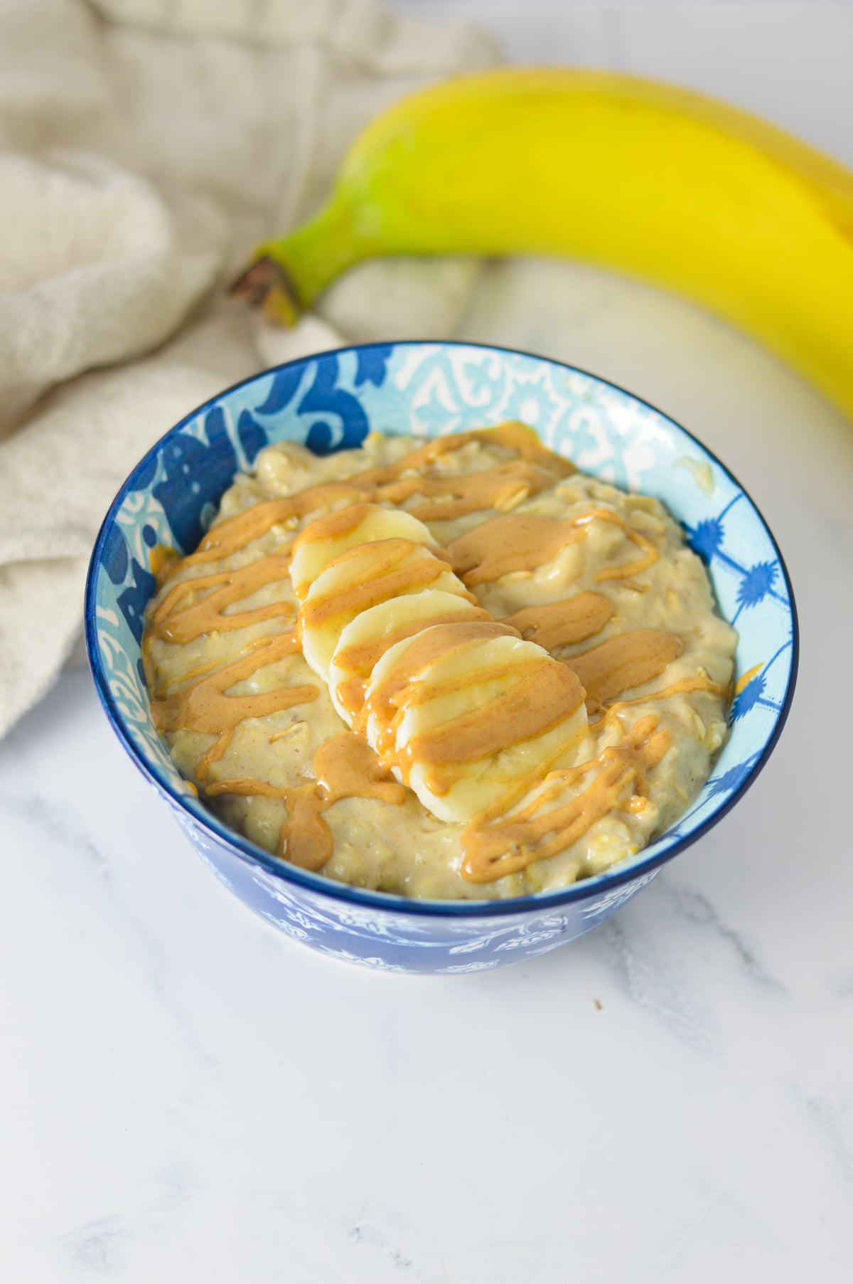 A bowl of warm peanut butter and banana oatmeal topped with sliced bananas and a drizzle of peanut butter.